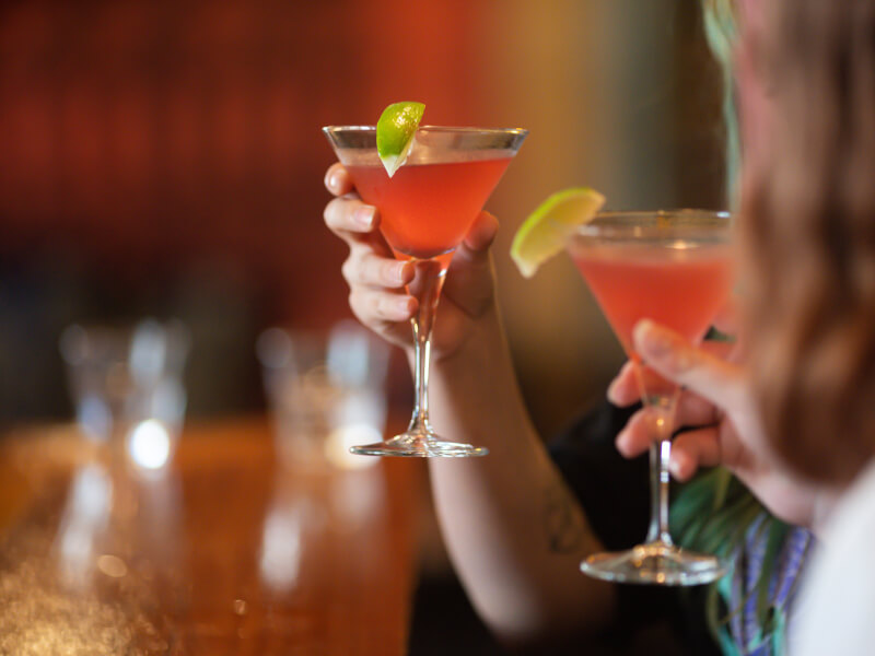 Two people hold up the drinks they made in a cocktail masterclass.